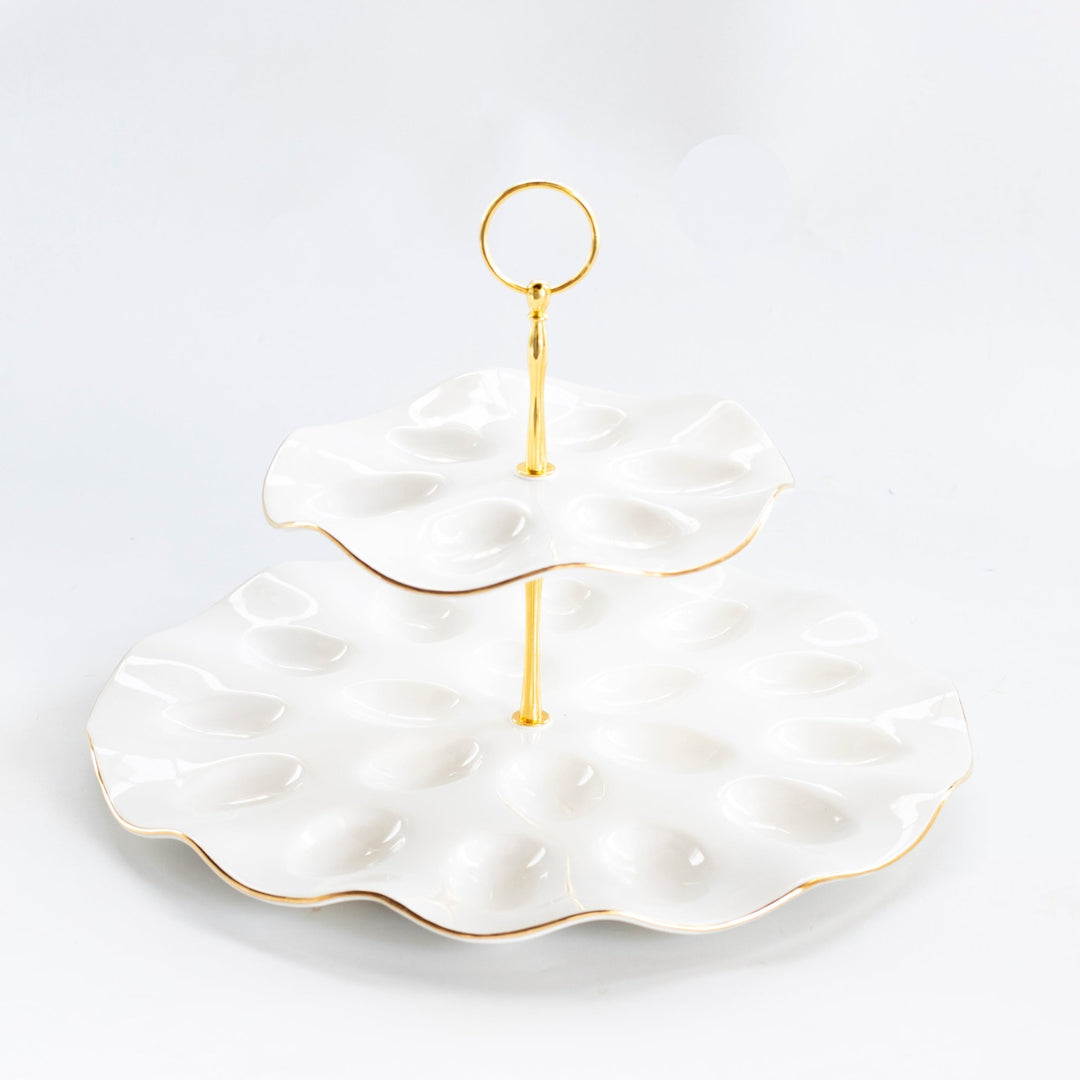 Two tier white stoneware deviled egg platter with scalloped egg wells, gold rims, and a gold ring handle