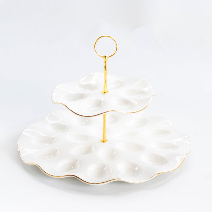 Two tier white stoneware deviled egg platter with scalloped egg wells, gold rims, and a gold ring handle