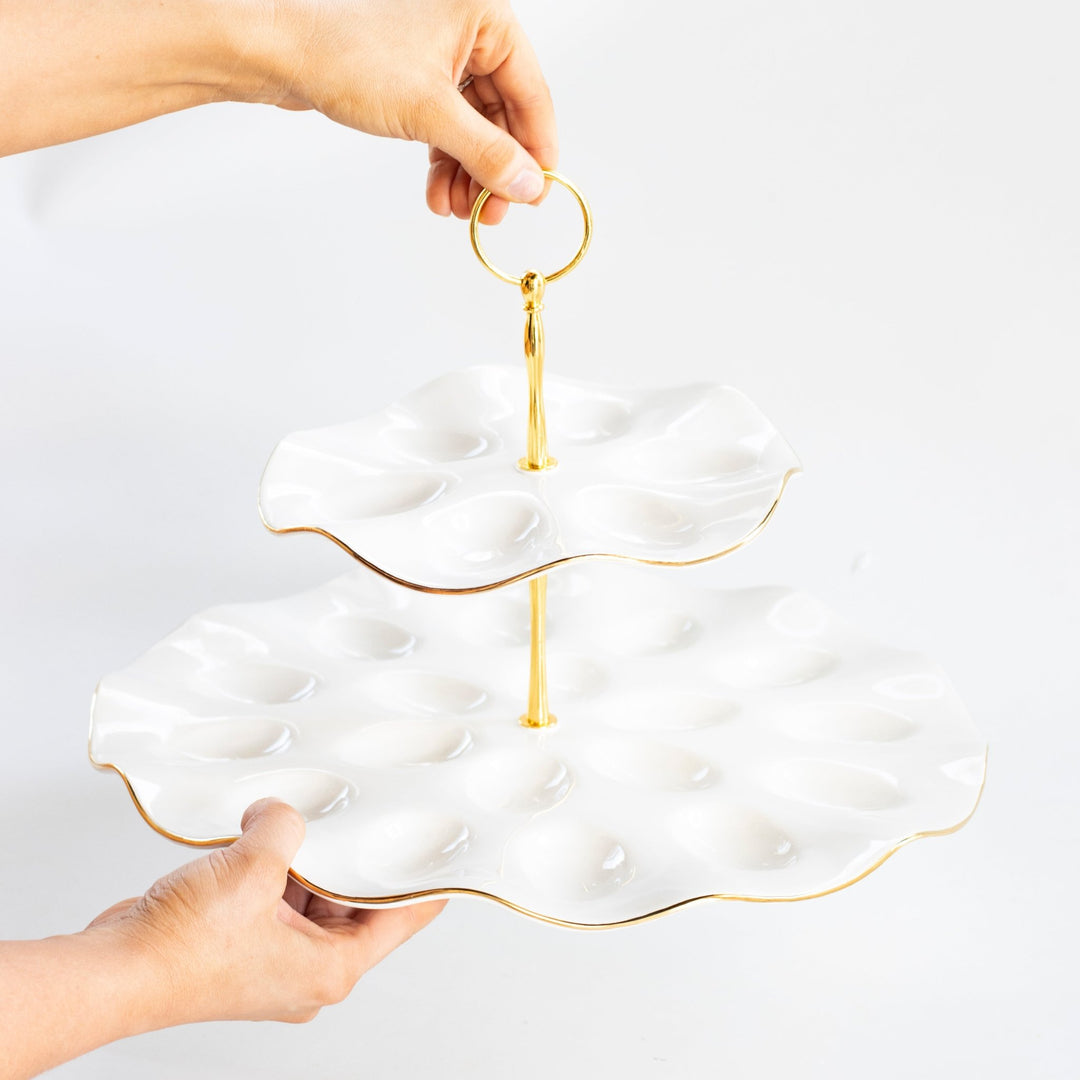 Hands lifting the tiered deviled egg platter by its gold ring handle