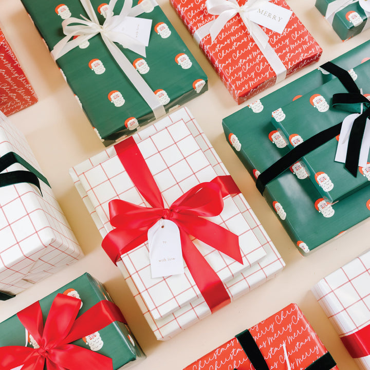 Overhead rows of Santa face, red grid, and Merry Christmas script gifts with satin and velvet bows