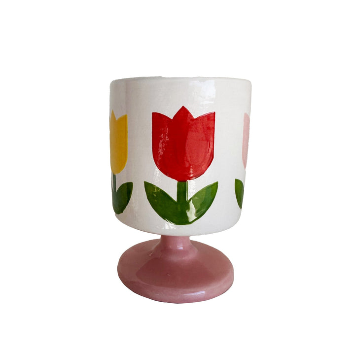White footed ceramic cup painted with red and yellow tulips and green leaves on a pink pedestal base