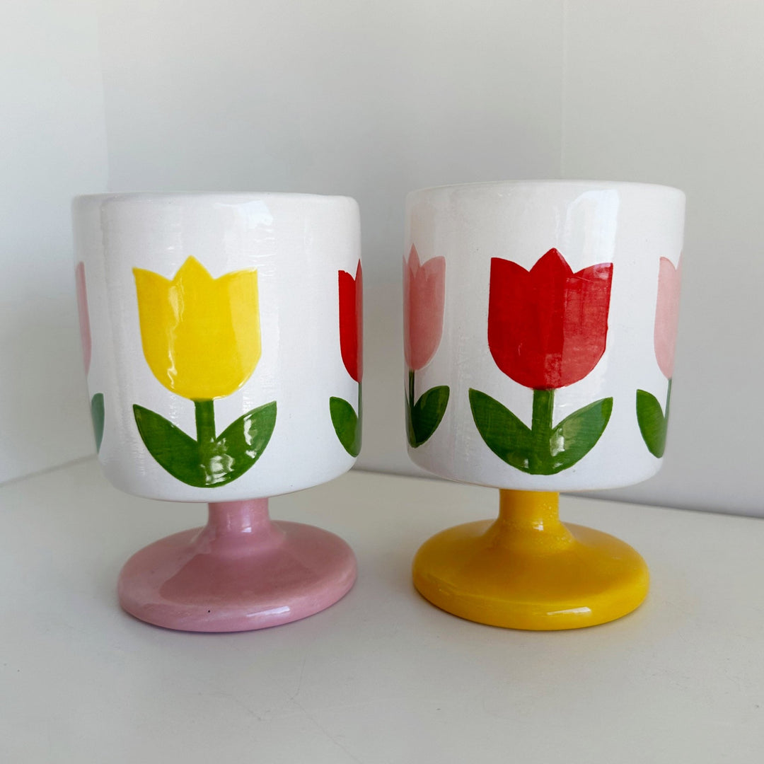 Pair of white ceramic tulip cups with red and yellow tulips, one on a pink pedestal base and one on a yellow base