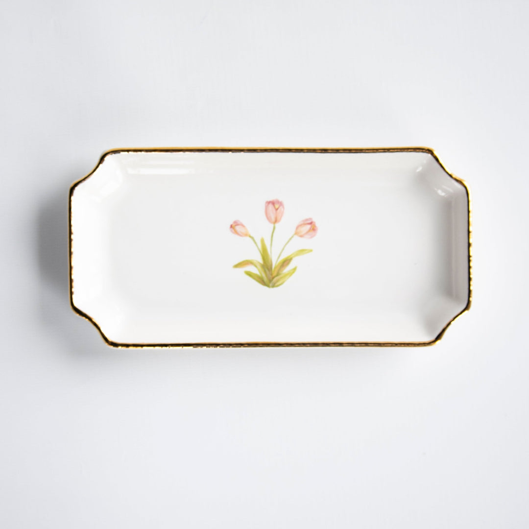 White ceramic petite valet tray with notched corners, gold rim, and a pink tulip painted in the center