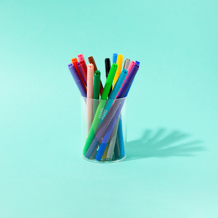 Ultra-washable markers standing in a cup on a teal background