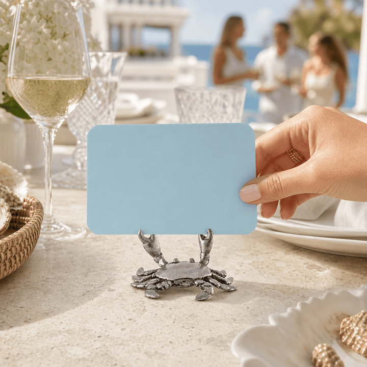 Hand setting a blue card into a pewter crab place card holder at a seaside dinner party