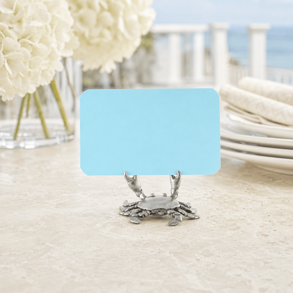 Pewter crab place card holder with a blue card on a coastal table with white hydrangeas