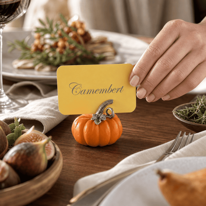 Hand setting a Camembert card into the orange pumpkin place card holder beside a bowl of figs