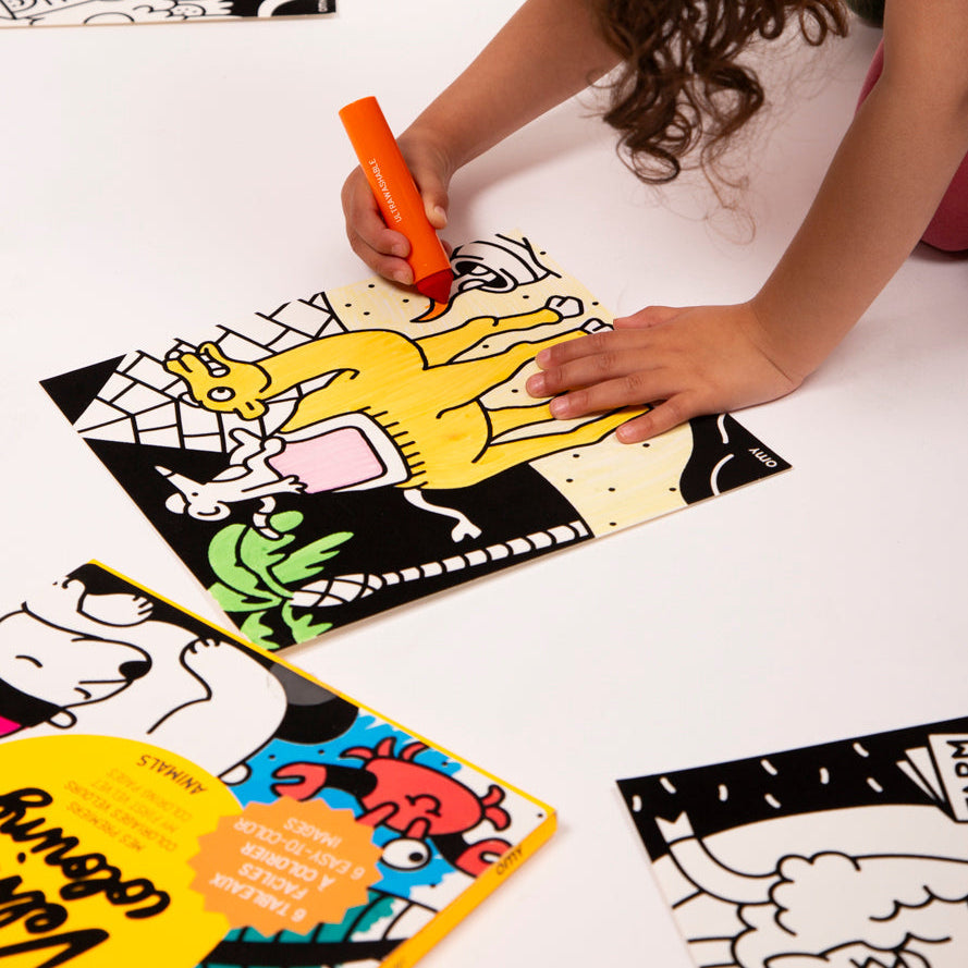 Child's hand coloring a black velvet animal panel with an orange marker