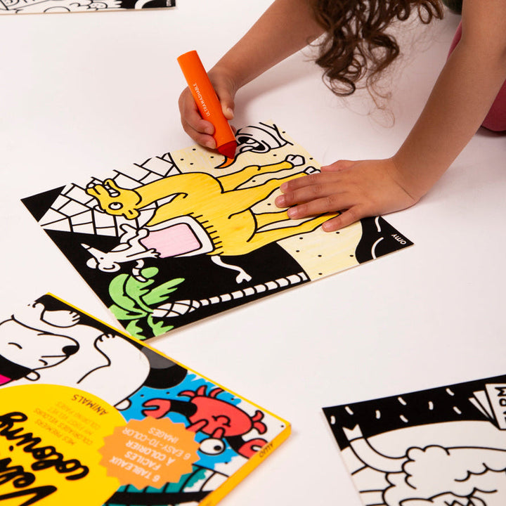 Child's hand coloring a black velvet animal panel with an orange marker