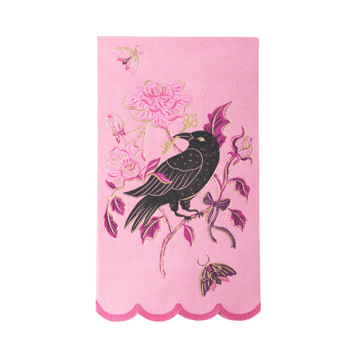 A pink decorative paper napkin with a scalloped bottom edge, featuring a black bird perched on a branch with pink flowers and gold accents.