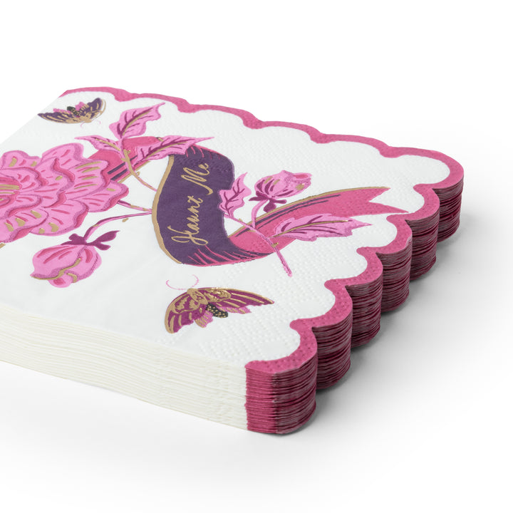 A stack of white paper napkins with scalloped edges, decorated with pink floral designs, butterflies, and a purple banner reading 'Haunt Me'.