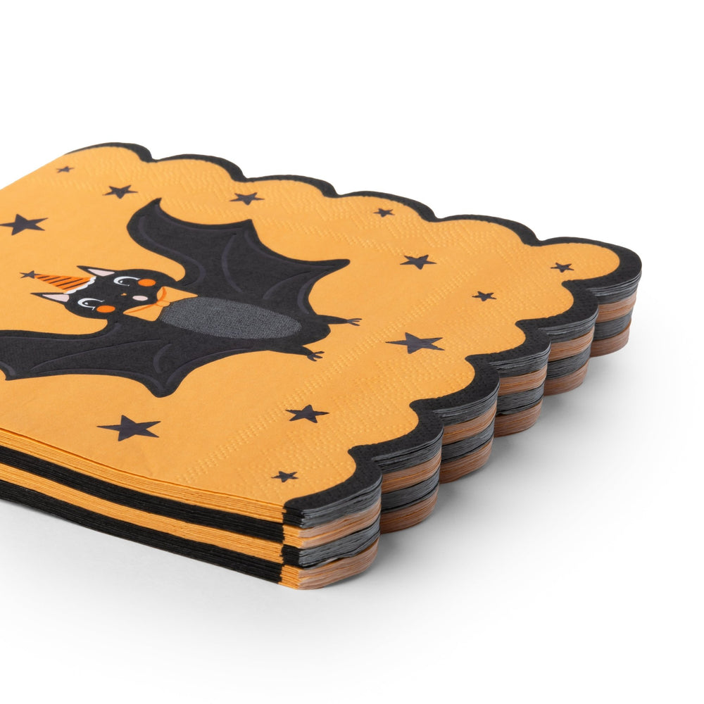A stack of Halloween-themed paper napkins with a scalloped edge, featuring a black bat on a textured orange background with black stars, photographed on a white studio background.