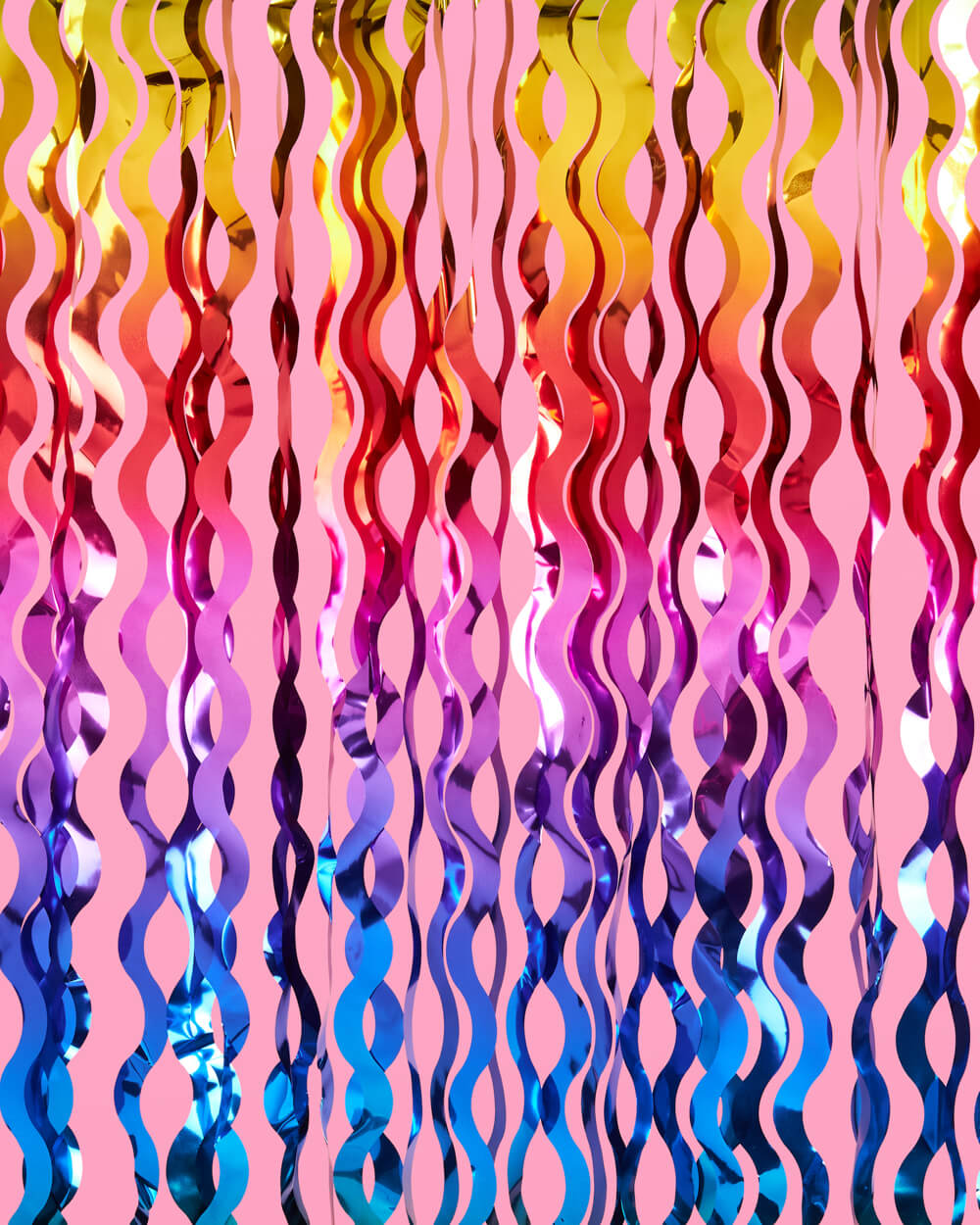 Rainbow wavy cut foil curtain in blue, purple, red, and gold hung as a party backdrop