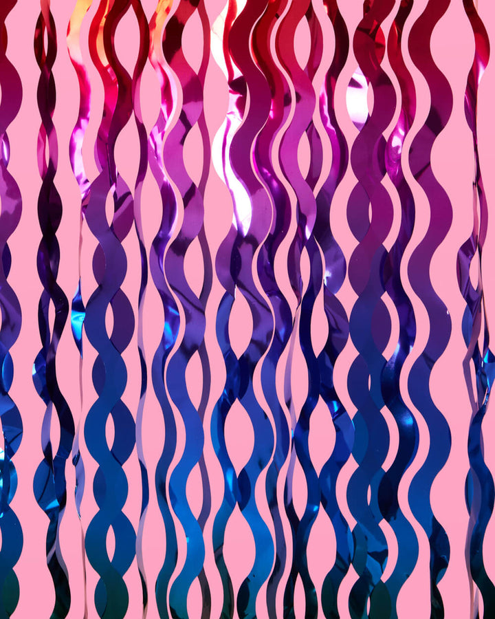 Blue and purple wavy foil curtain strands rippling against a pink background