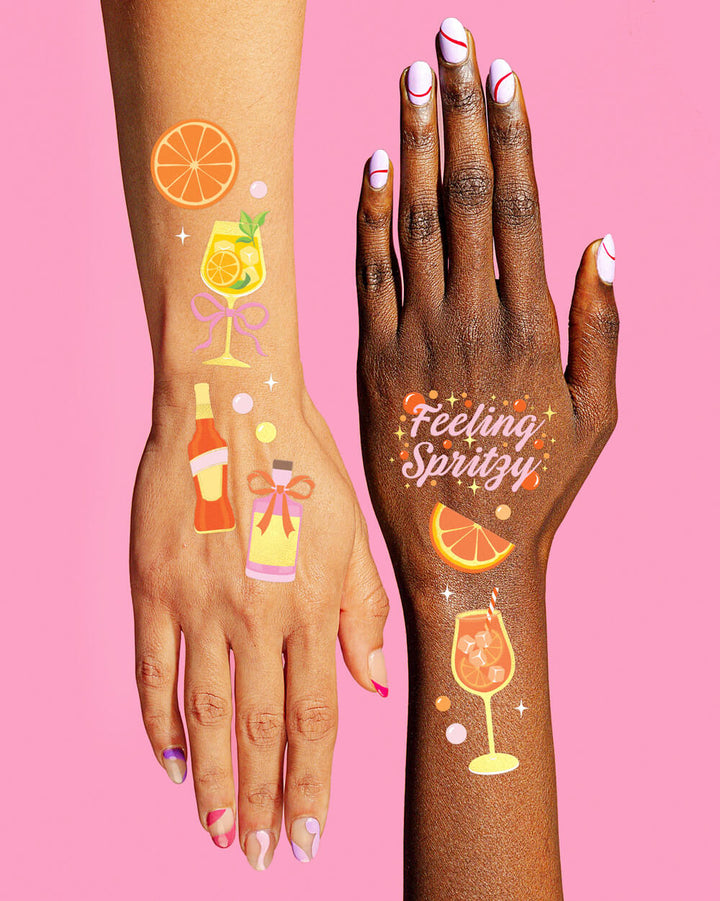 Arm and hand wearing Feeling Spritzy temporary tattoos with spritz glasses and an orange slice
