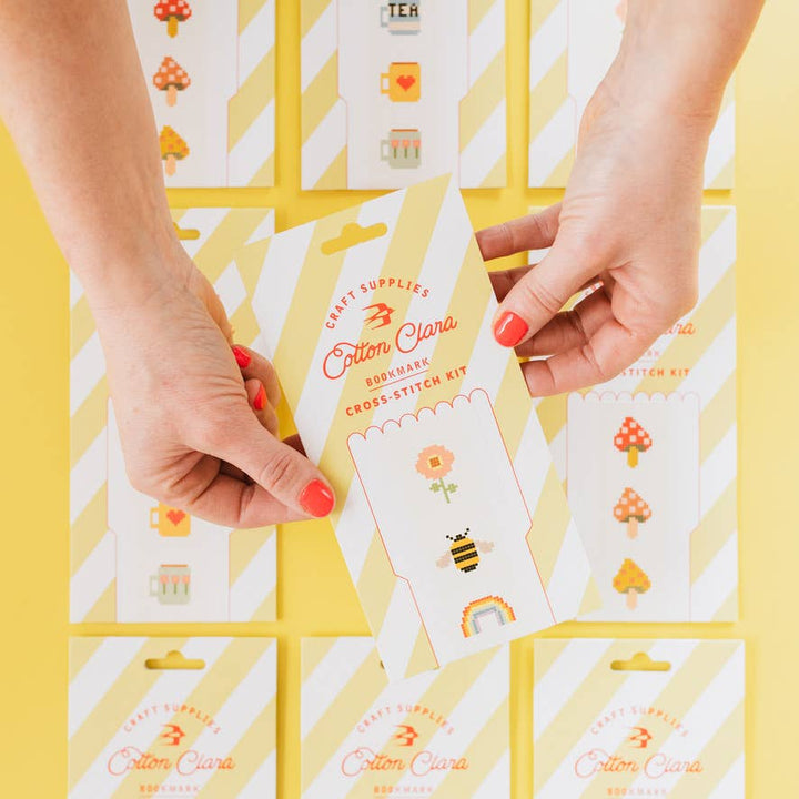 Hand holding a Cotton Clara bookmark cross stitch kit packet on a yellow background