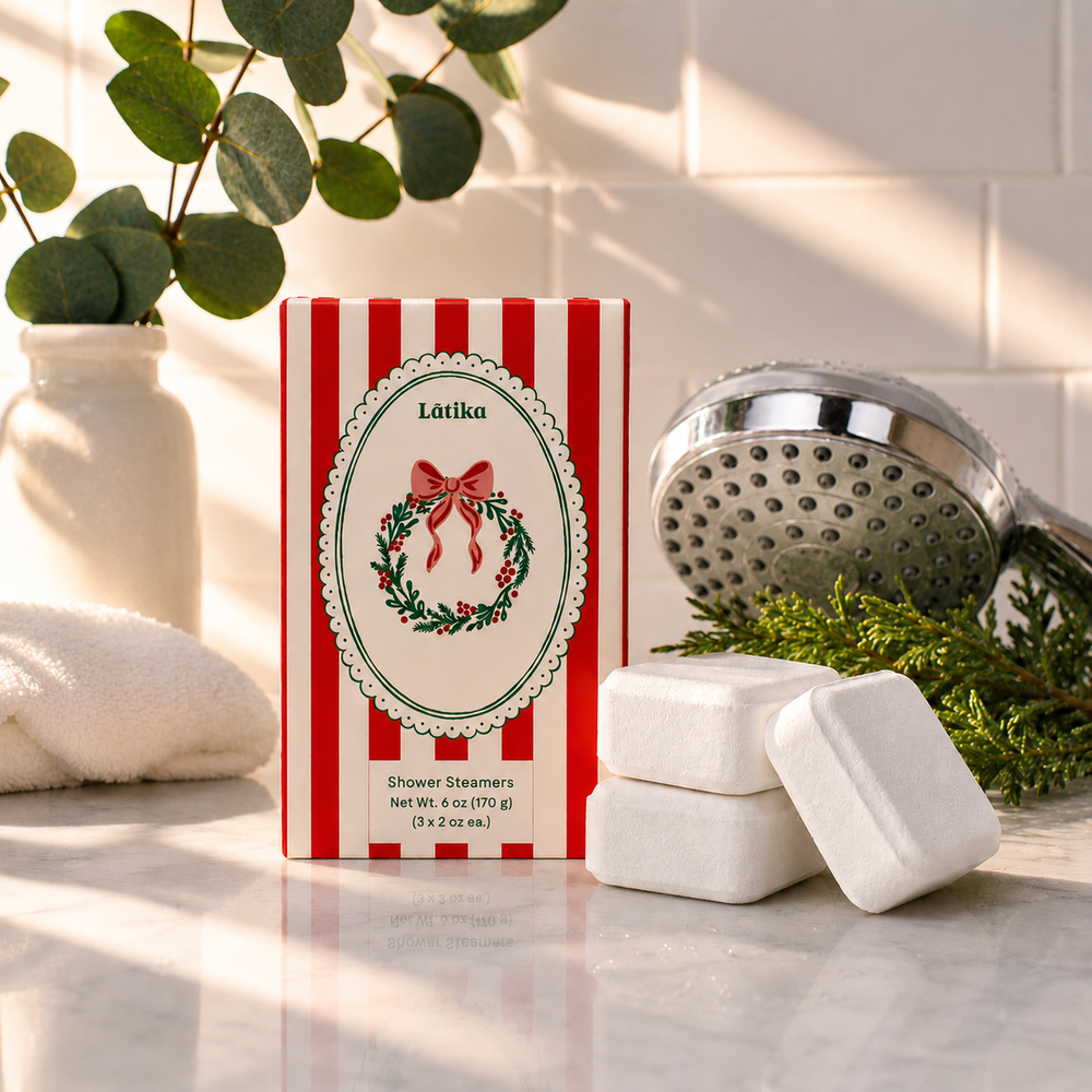 Red striped wreath box with three white shower steamer cubes by a shower head, a holiday spa upgrade