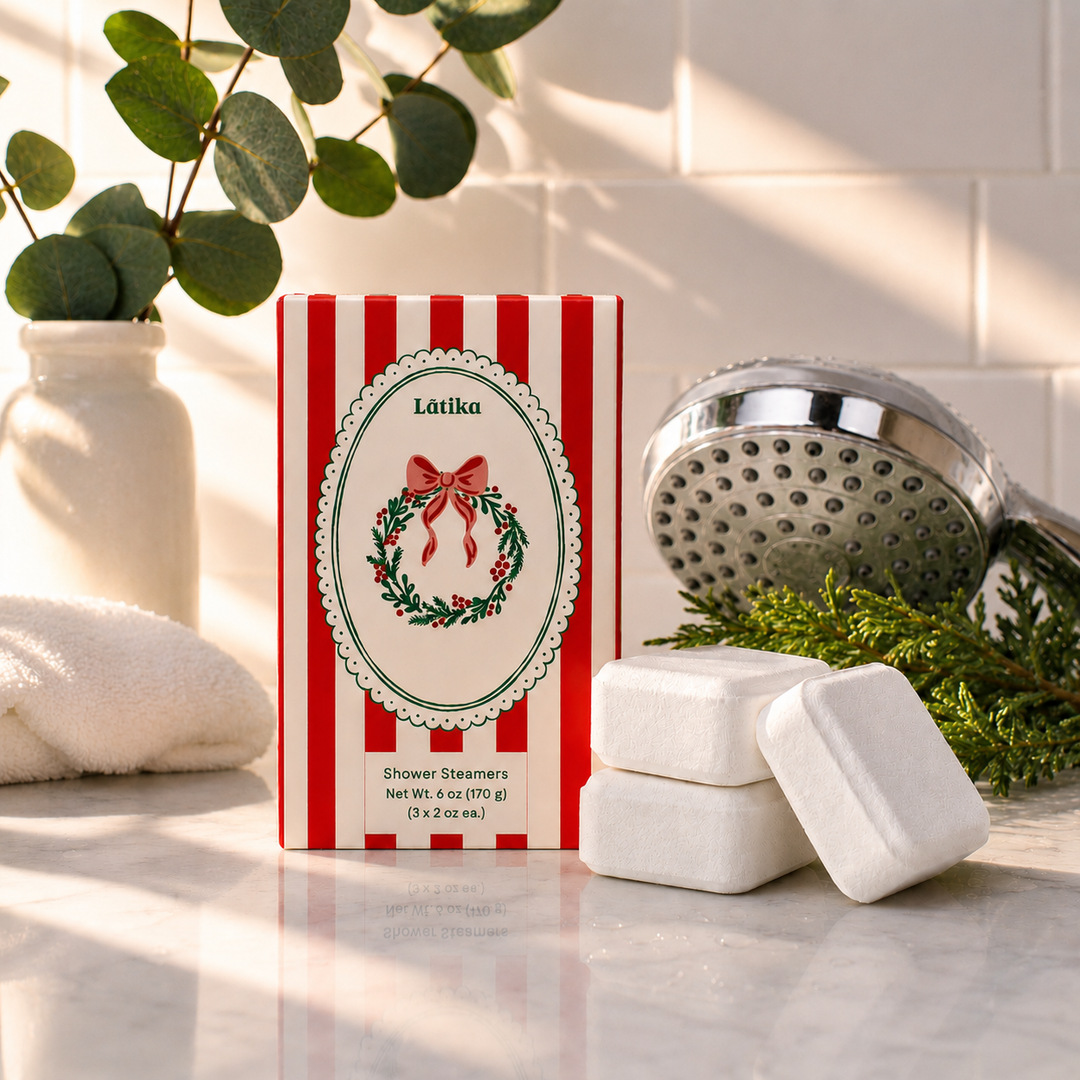 Red striped wreath box with three white shower steamer cubes by a shower head, a holiday spa upgrade