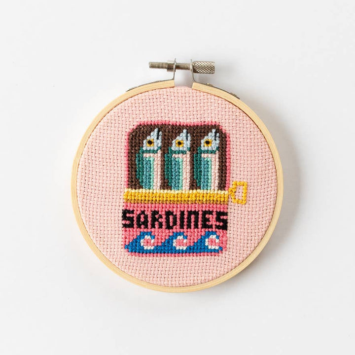 Close view of the sardine tin cross stitch design with three fish on pink fabric
