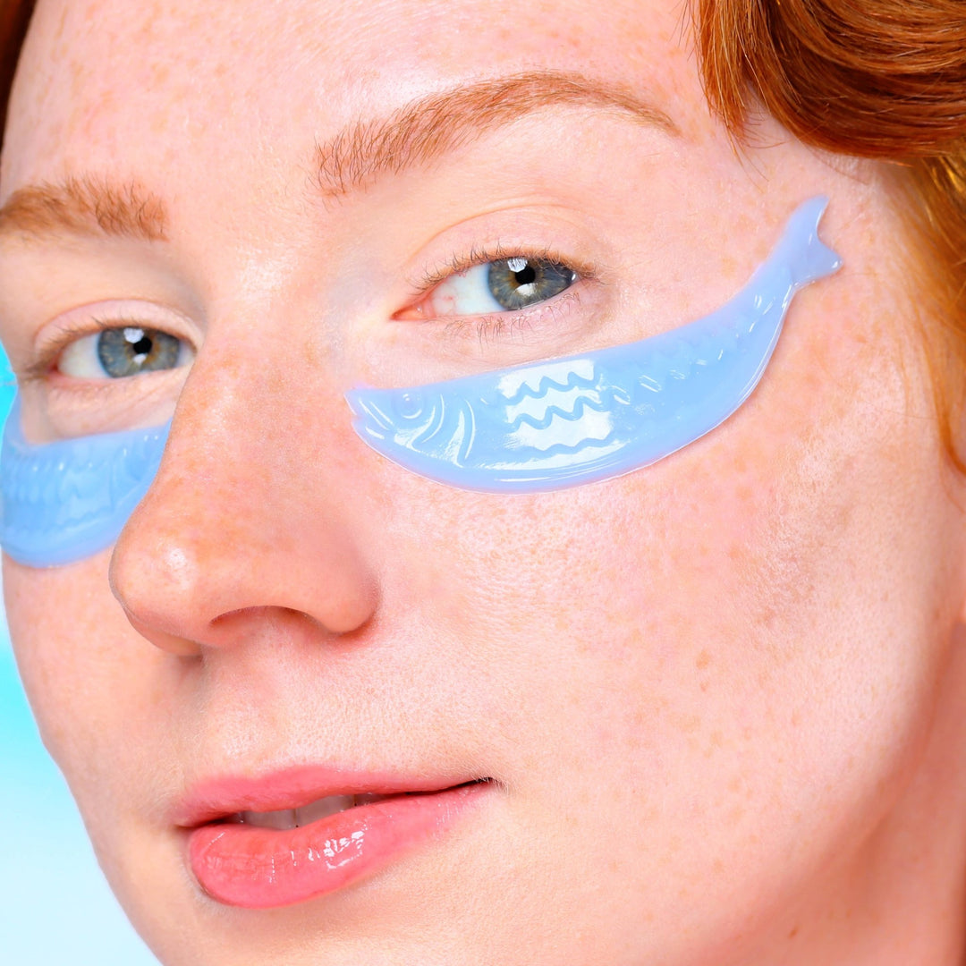 Close up of blue fish shaped hydrogel patches under the eyes showing scale texture, quirky depuffing skincare