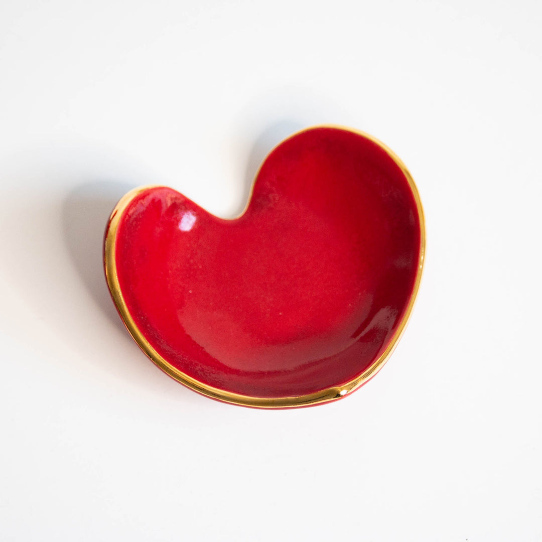 Glossy red heart ring dish with a gold rim, angled view on white