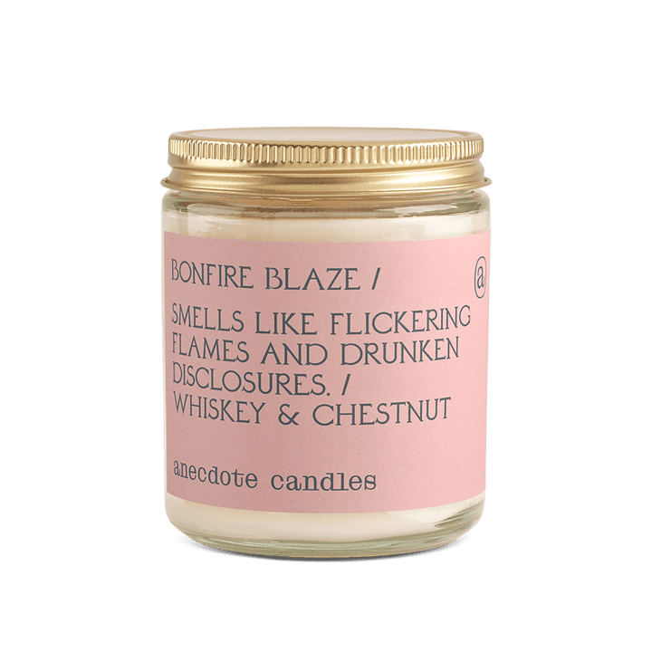 Bonfire Blaze whiskey and chestnut candle in a clear glass jar with a blush pink label and gold lid