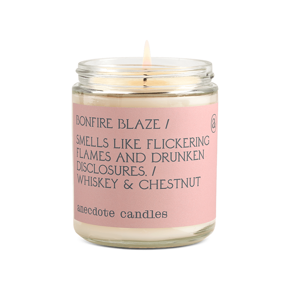 Lit Bonfire Blaze glass jar candle with a blush pink label reading whiskey and chestnut