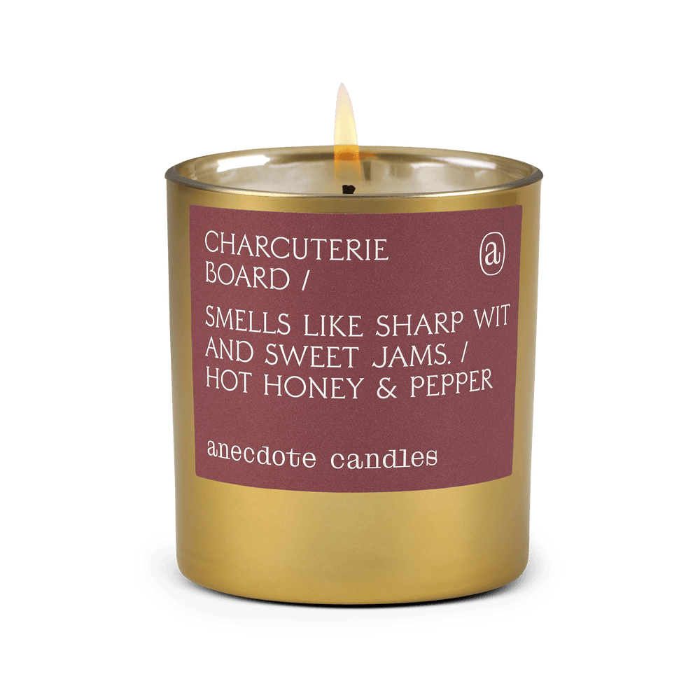 Lit gold tumbler candle with a plum Charcuterie Board label reading hot honey and pepper