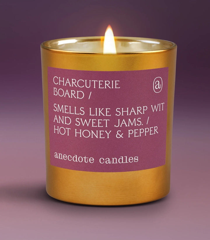 Lit Charcuterie Board candle in a gold tumbler with a plum hot honey and pepper label against purple