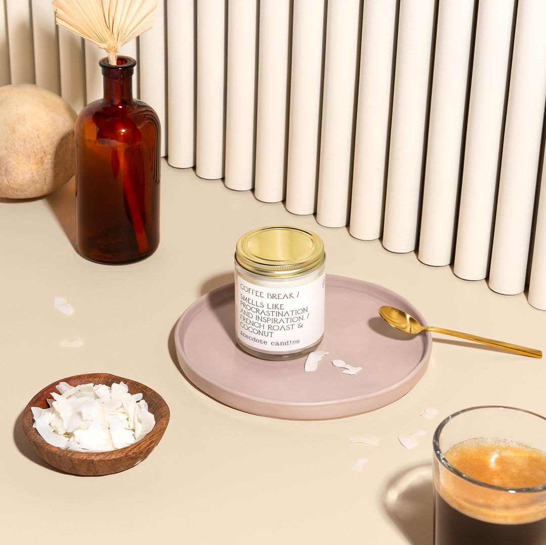 Lidded Coffee Break candle on a pink tray with a gold spoon, coconut flakes, and a glass of espresso