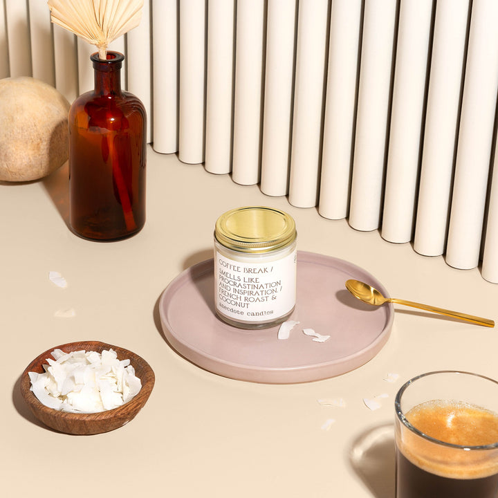 Lidded Coffee Break candle on a pink tray with a gold spoon, coconut flakes, and a glass of espresso
