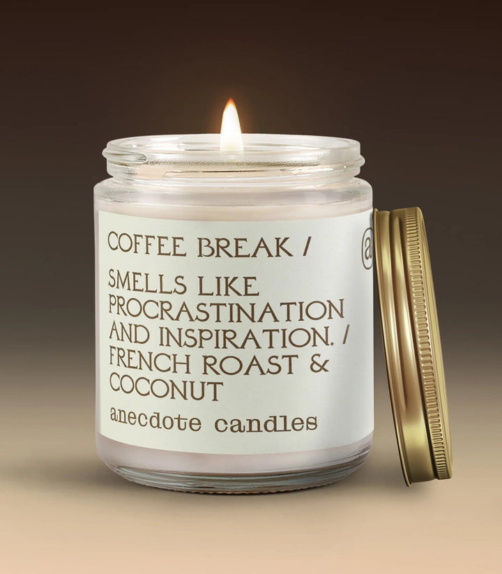 Lit Coffee Break French roast and coconut candle with a white label and gold lid leaning beside the jar