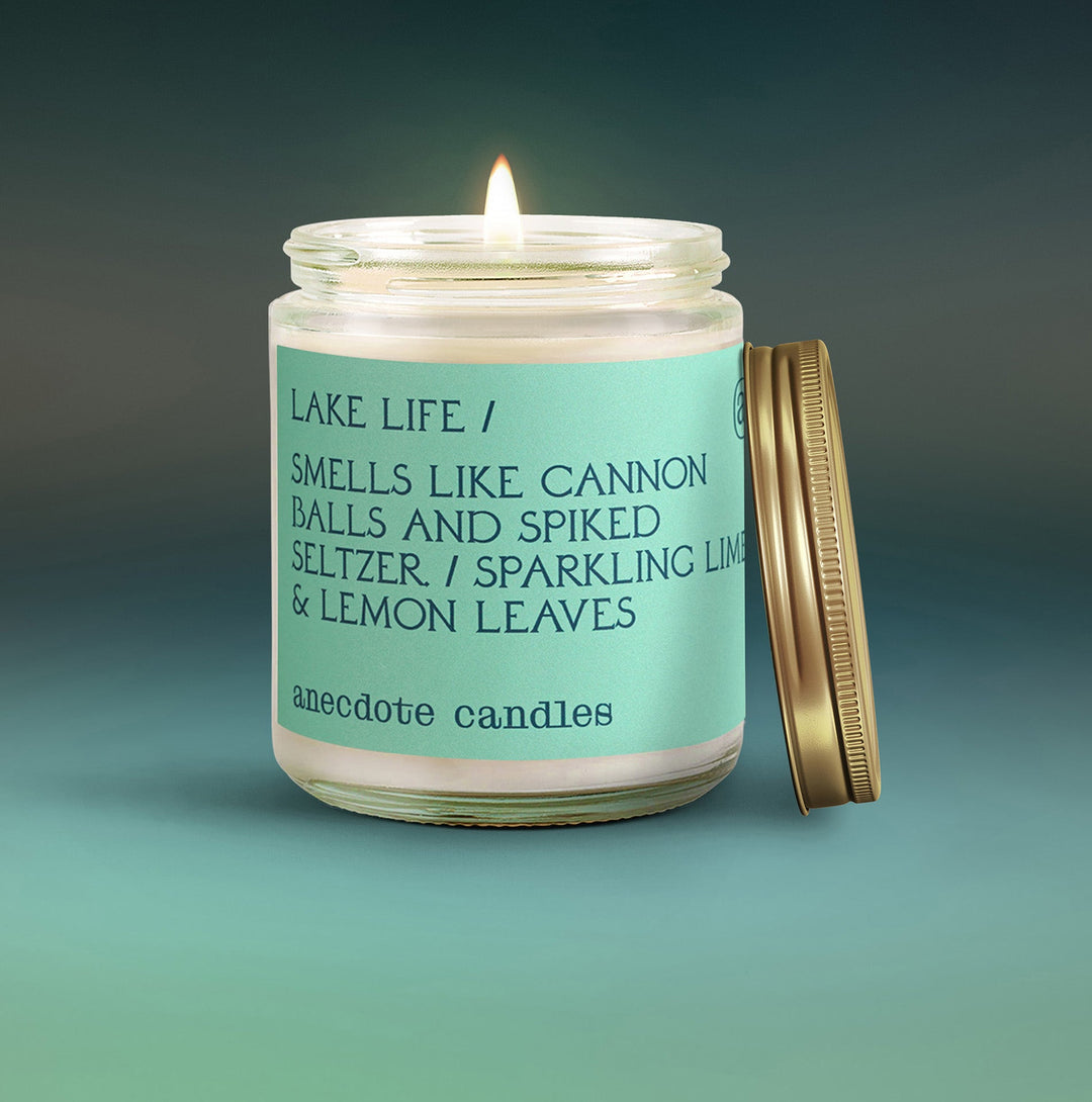 Lit Lake Life candle with a mint green sparkling lime and lemon leaves label and gold lid leaning beside the jar