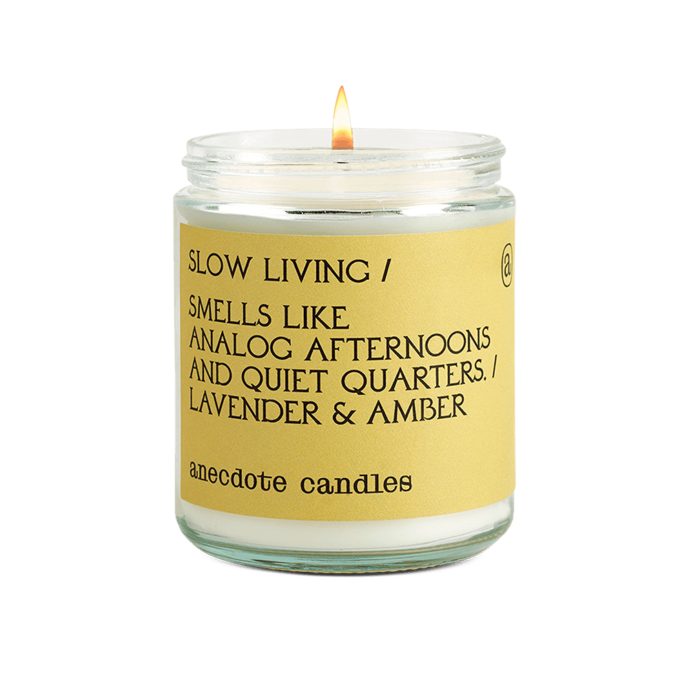 Lit Slow Living glass jar candle with a yellow label reading lavender and amber