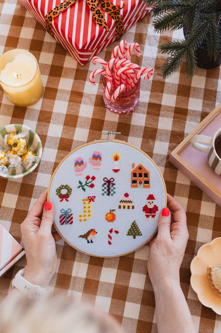 Holding the Christmas cross stitch sampler over a brown gingham table with candy canes