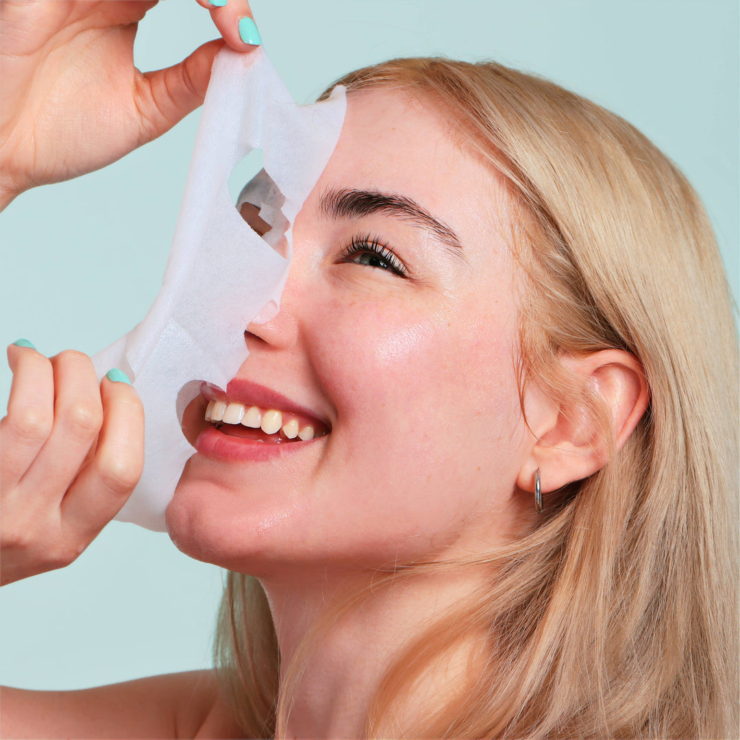 Smiling model peeling off the sheet mask to reveal glowing skin after a Christmas pamper session