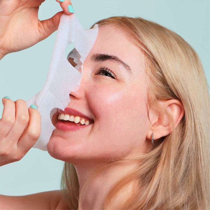 Model peeling away the sheet mask with a laugh, fresh glowing skin ready for the holiday party