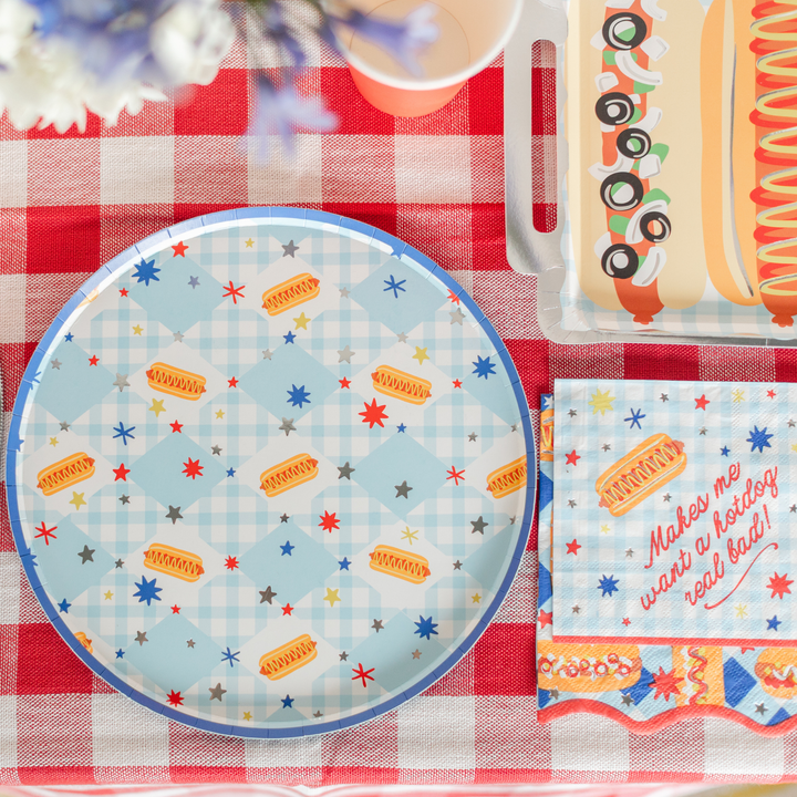 Hot dog party plates and platter styled with napkins on a red gingham cookout table