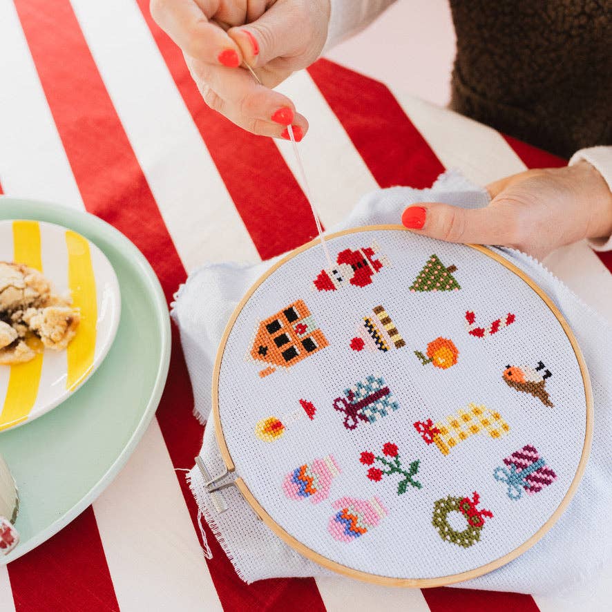 Hands stitching the colorful Christmas sampler with Santa and tree motifs