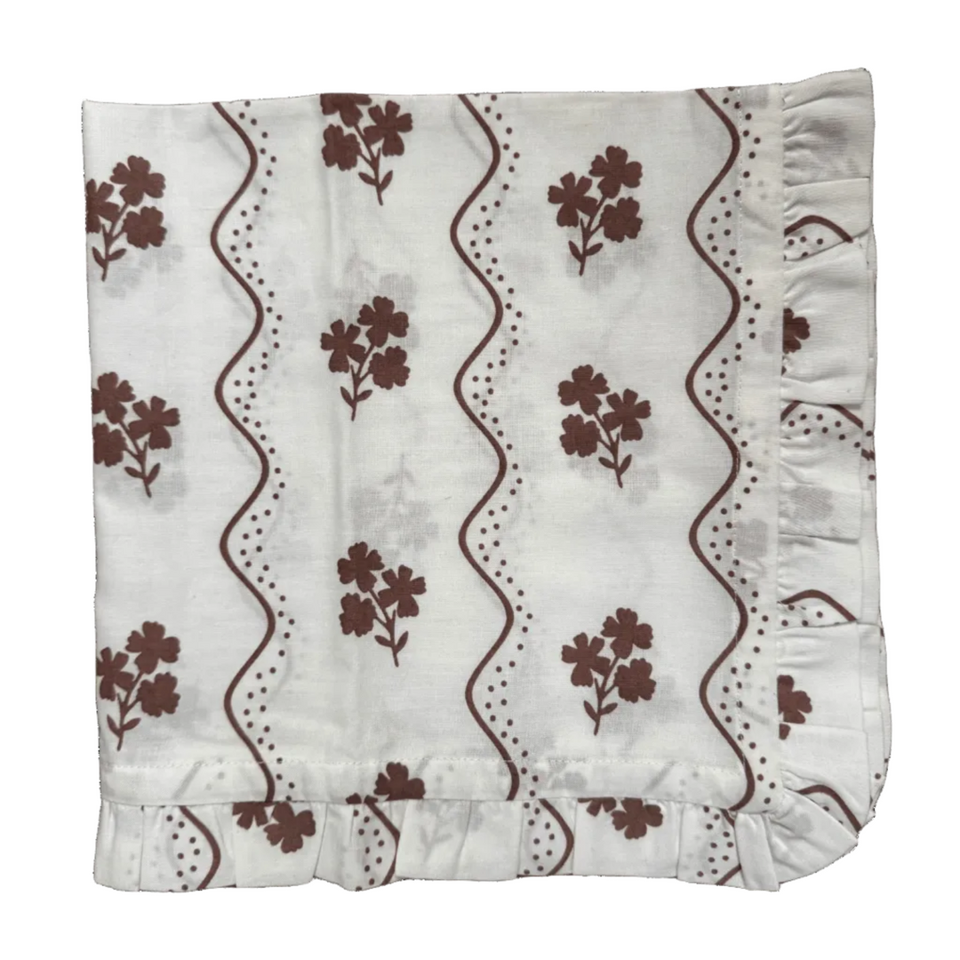 White fabric with brown floral patterns and ruffled edges on a green background