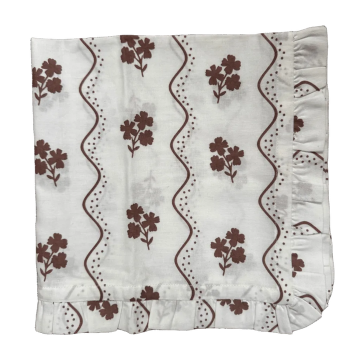 White fabric with brown floral patterns and ruffled edges on a green background