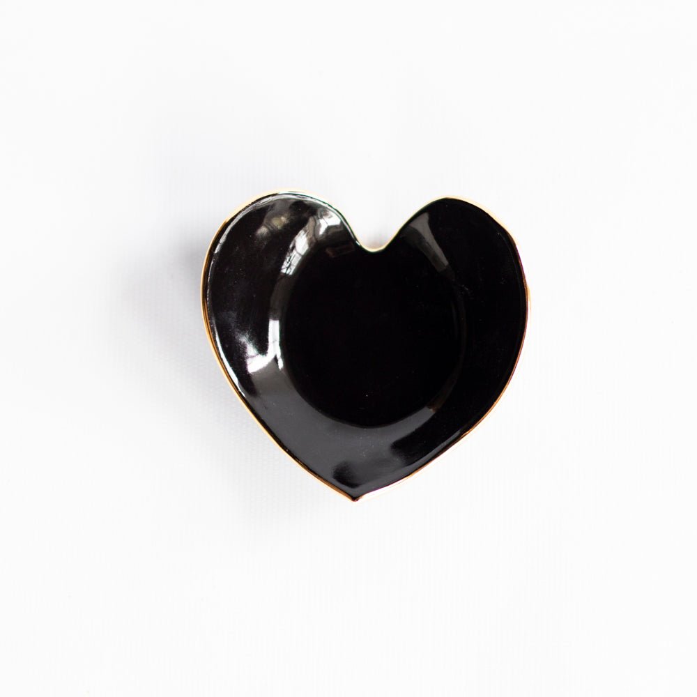 Glossy black heart ring dish with a gold rim on white