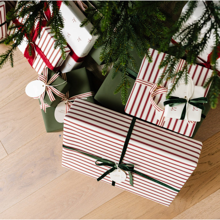 Red striped and bow print presents tied with green velvet ribbon under Christmas tree branches