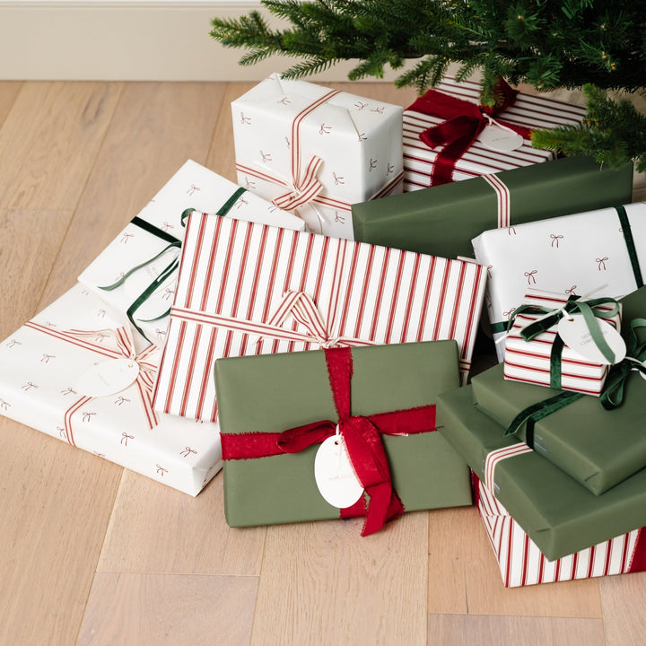 Bow print and striped Christmas gifts piled on a wood floor at the foot of the tree