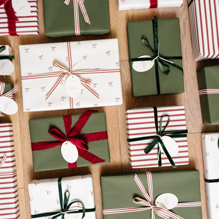 Top-down grid of bow print, candy stripe, and green wrapped gifts with velvet bows on wood