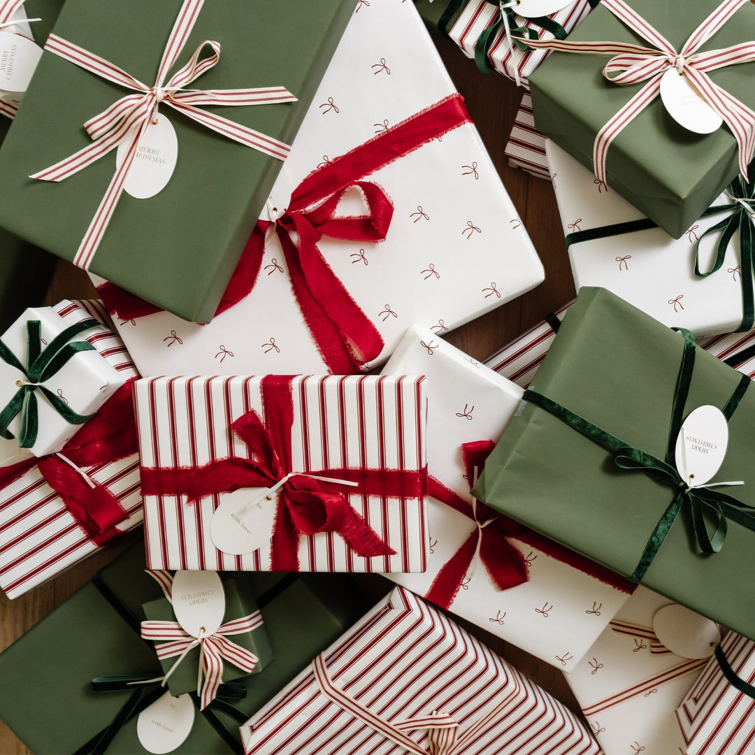 Overhead heap of Christmas gifts in small bow print, red stripe, and green paper with oval tags