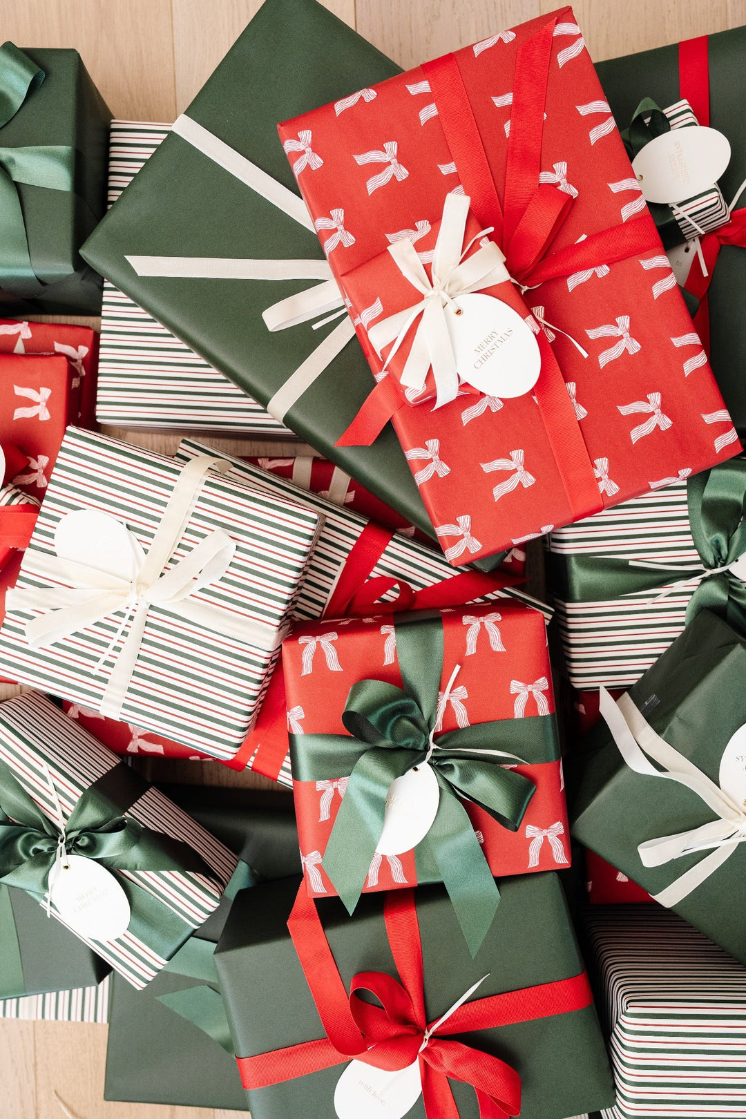 Top-down heap of holiday gifts in red bow print and green paper with red satin and cream velvet ribbon