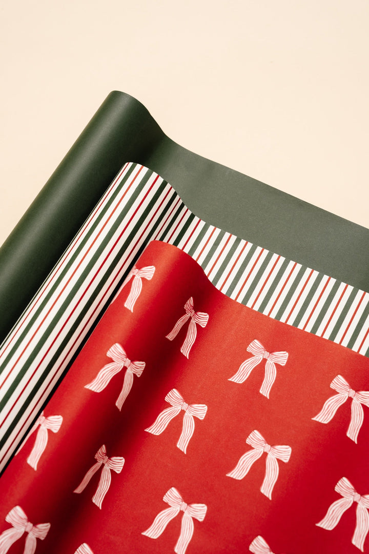 Rolls of solid green, red and green stripe, and red bow print wrapping paper unrolled on cream