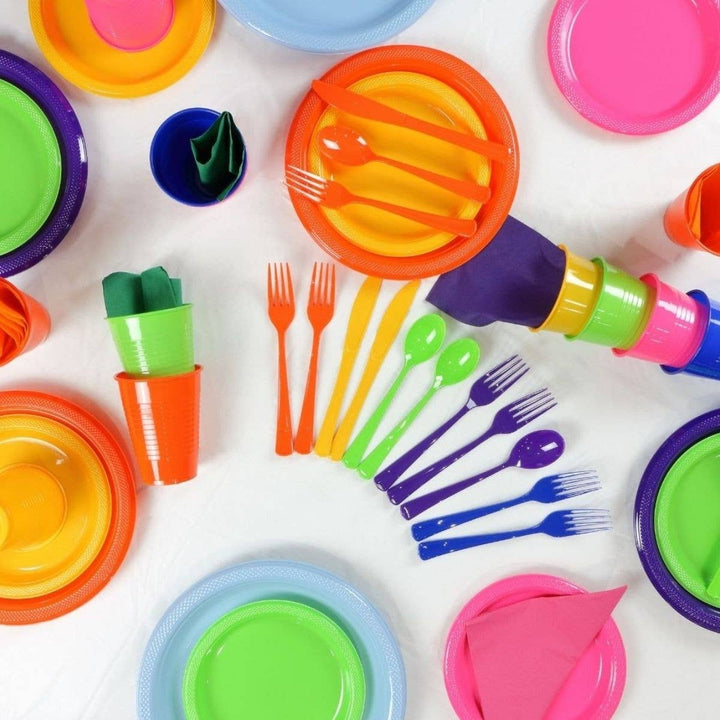 A colorful plastic party tableware set arranged on a white surface, including plates, cups, forks, knives, and spoons in bright neon shades of pink, blue, purple, green, orange, and yellow.