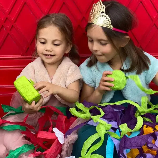 Two girls unwinding surprise balls in a pile of colorful crepe paper ribbons at a holiday celebration